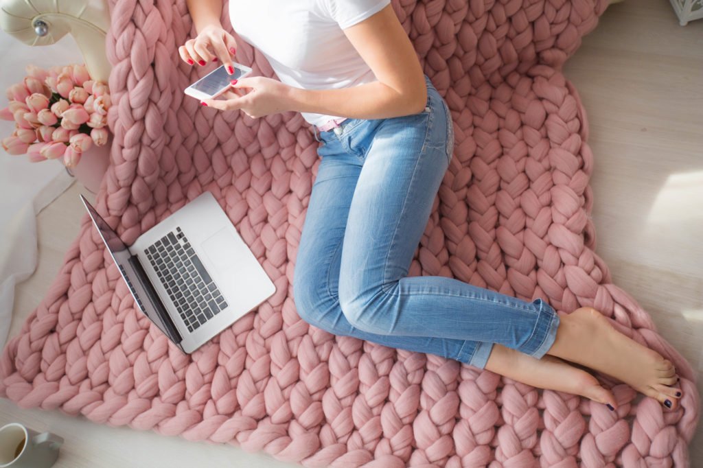 piernas de mujer en la cama con computadora portátil y teléfono: gane dinero rápido en línea